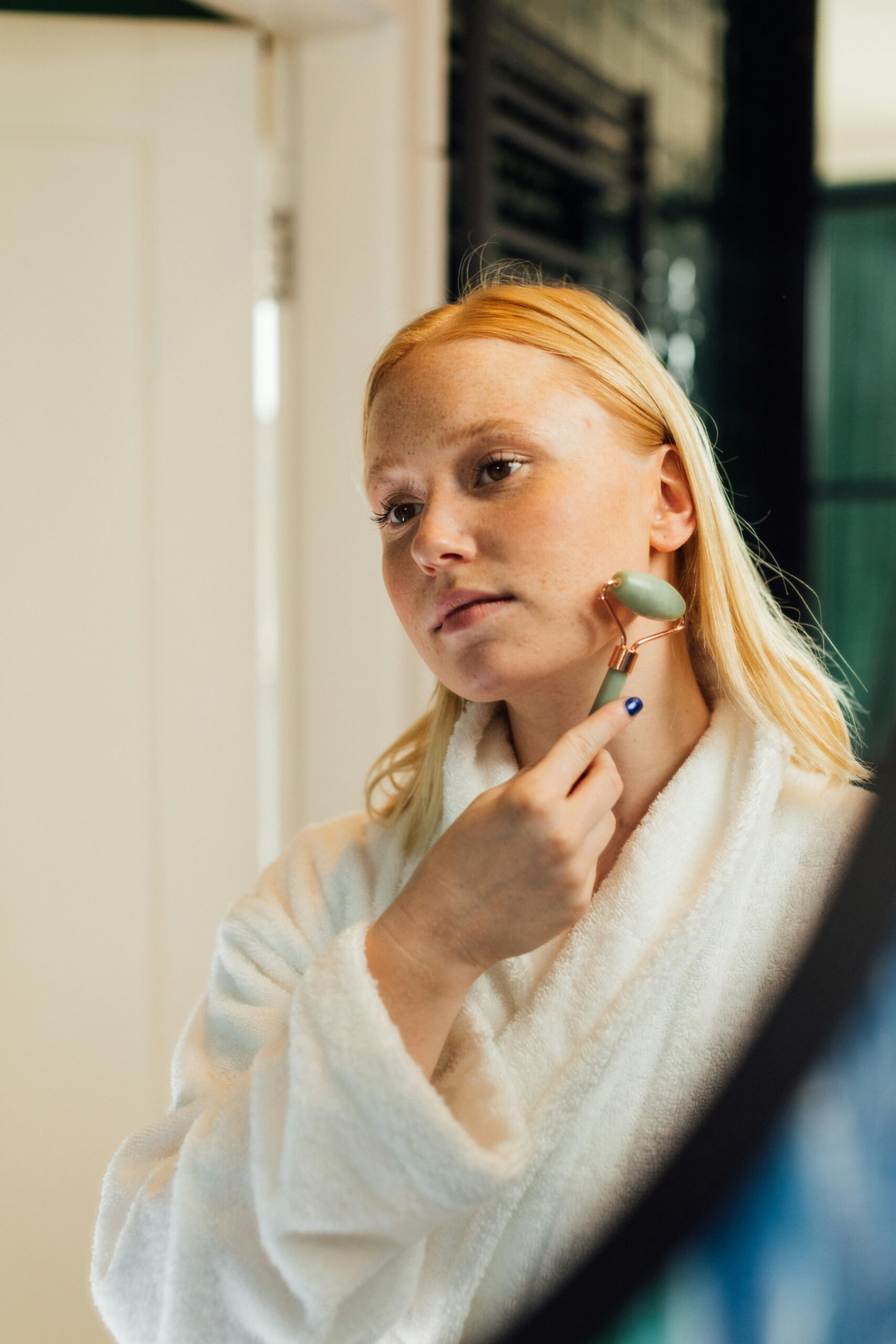Woman using jade roller for facial skincare routine indoors.